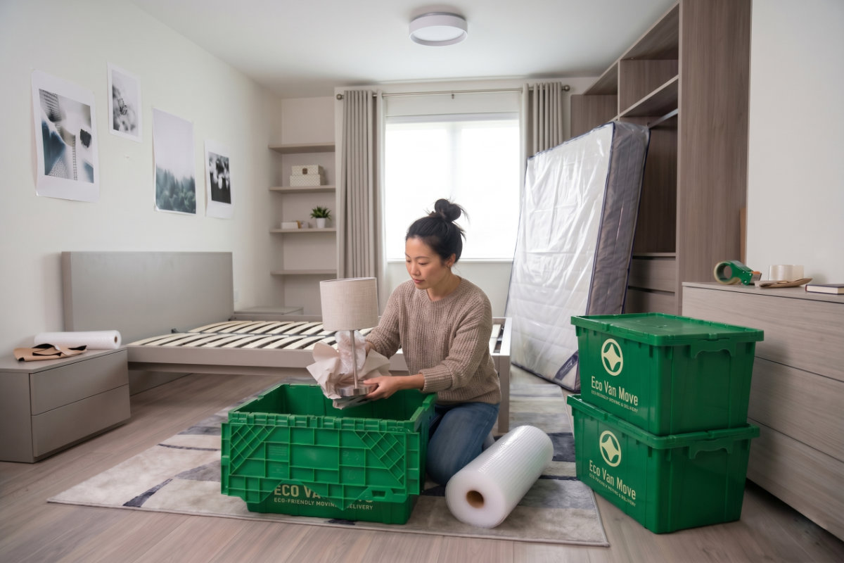 Woman packing a lamp into a green Eco Van Move reusable crate in a bedroom.