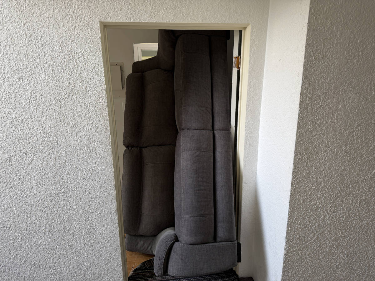 Large grey sofa being carefully moved through a narrow doorway during a residential furniture delivery.