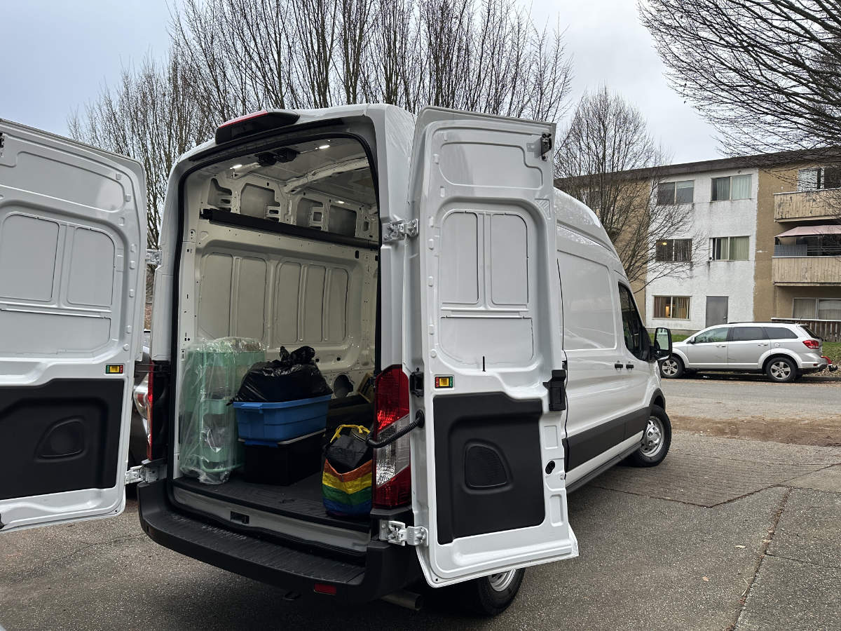 Open rear doors of a white moving van reveal a clean cargo area partially loaded with household items and reusable bins.
