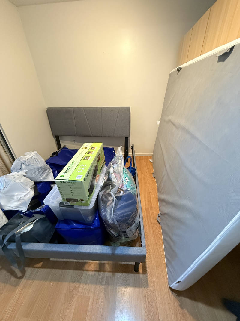 Packed moving boxes, bags, and a mattress sitting on a bed frame during a studio apartment move in Vancouver.