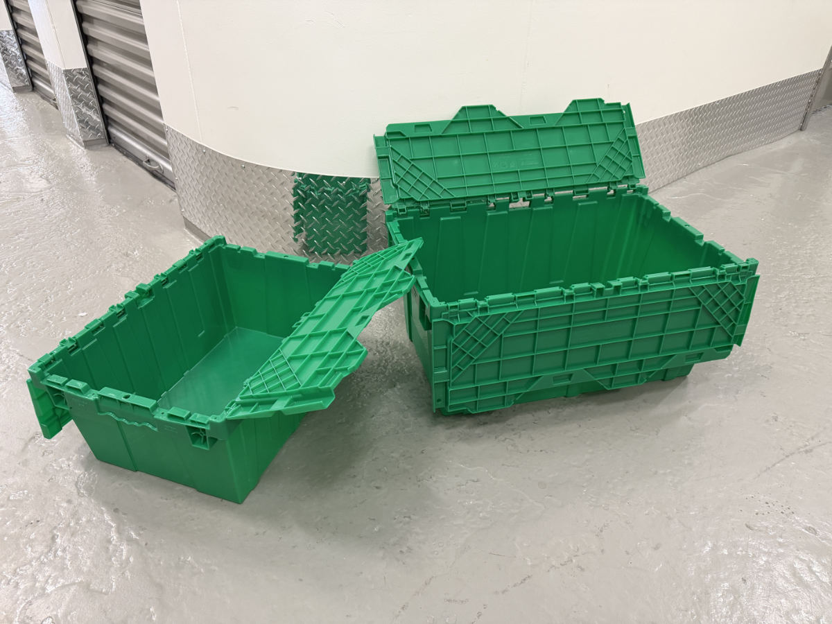 Two green plastic moving bins with attached lids open on a storage facility floor.