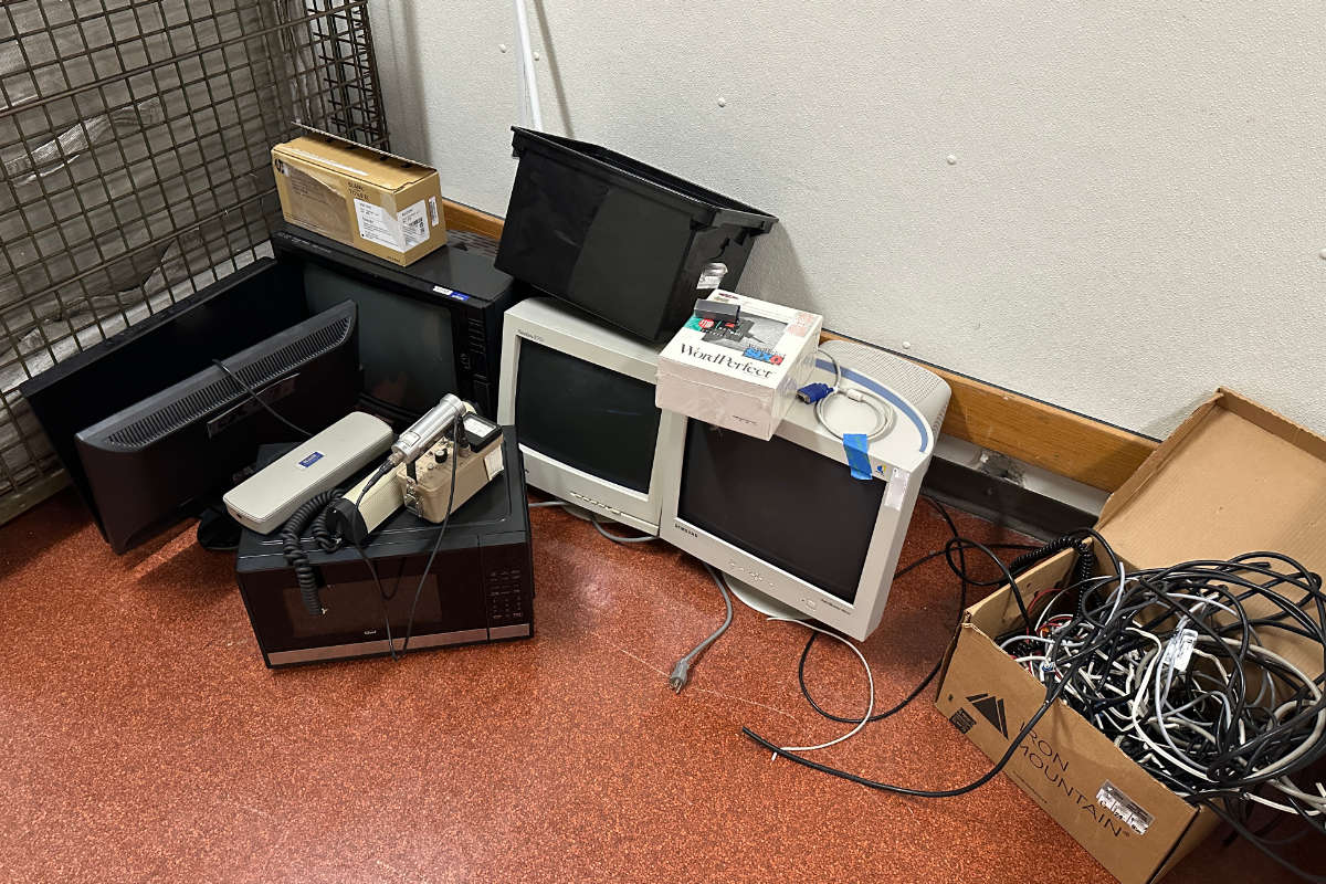 Old computer monitors, cables, and electronics piled together for e-waste recycling pickup in an office.