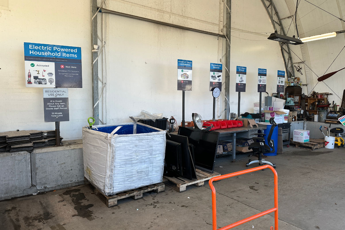 E-waste recycling drop-off area with labeled bins, old electronics, and sorting stations for household items.