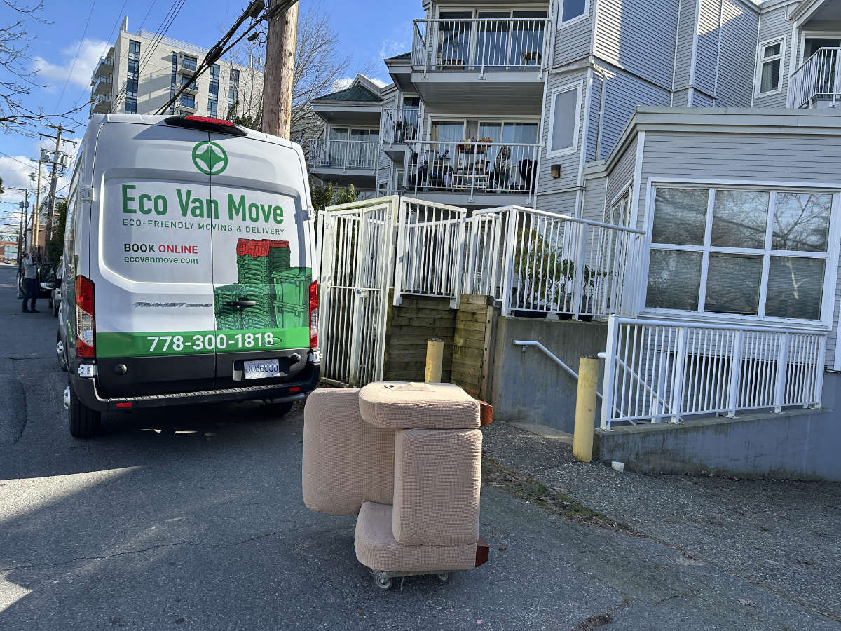 Eco Van Move delivery van parked outside an apartment building with a recliner on a dolly.