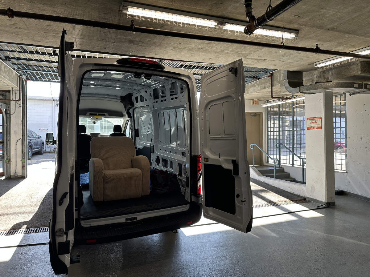 A beige recliner sits inside an open Eco Van Move delivery van parked in a garage.