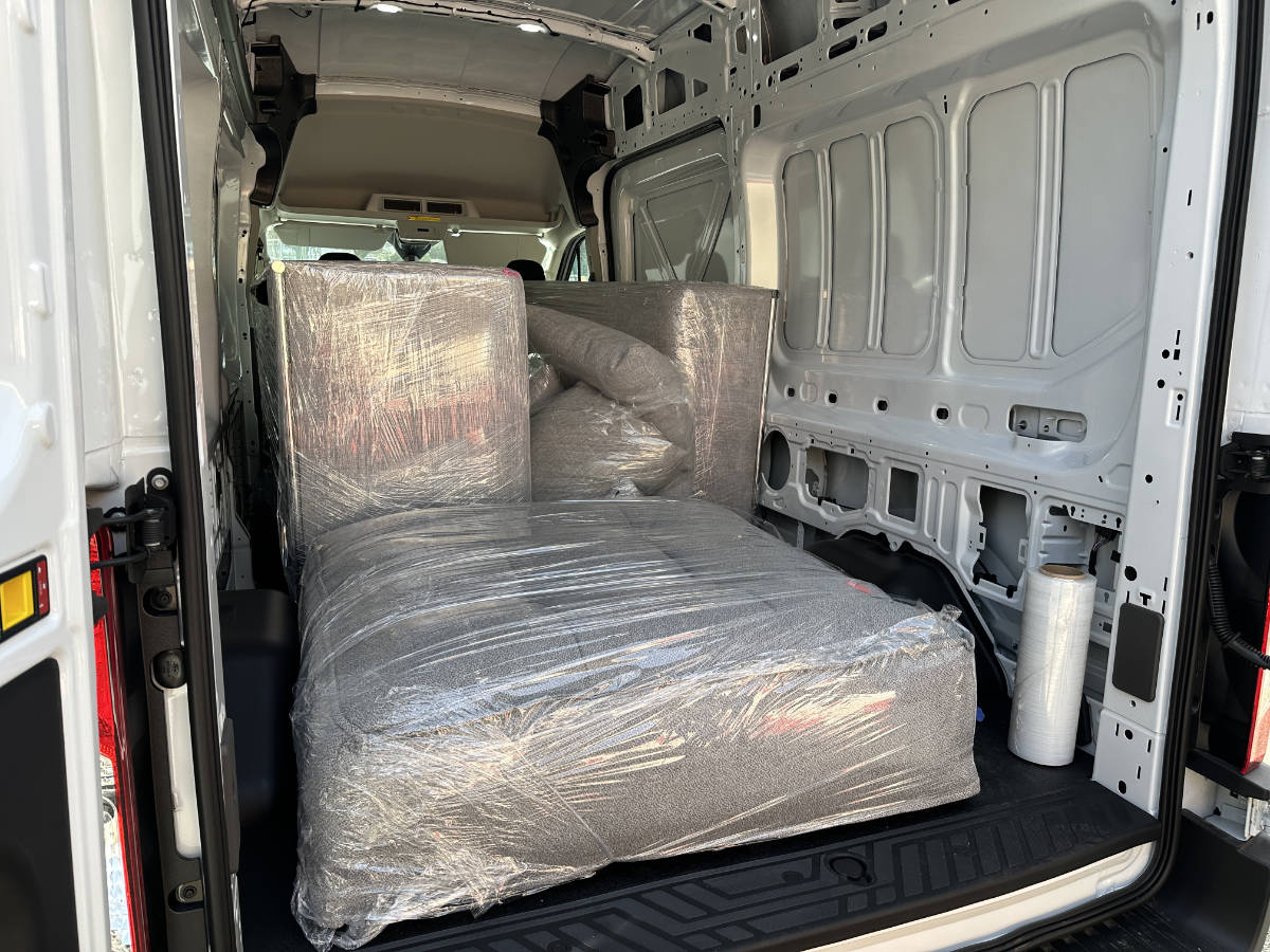 Plastic-wrapped sectional sofa loaded inside a white cargo van, ready for delivery.